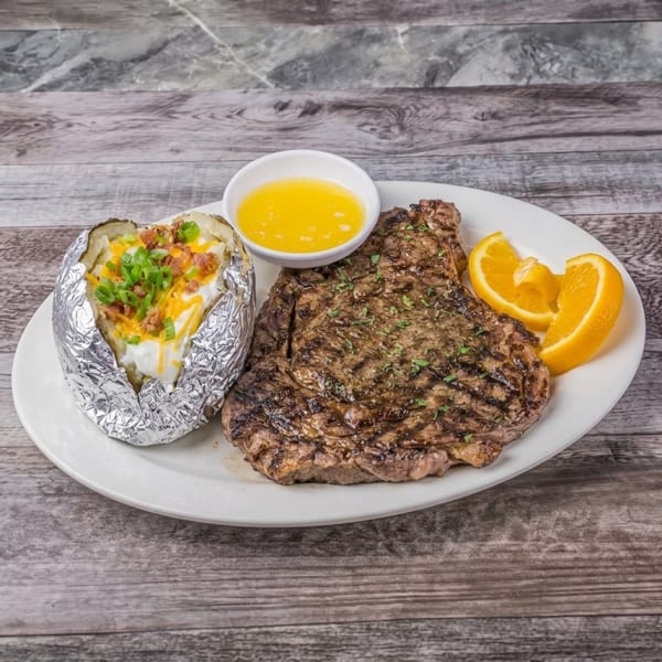 Loaded baked potato and grilled steak with melted butter and orange slices.