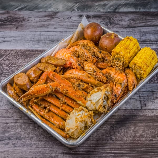 Seafood boil with crab legs, shrimp, sausage, corn, and potatoes on a metal tray.