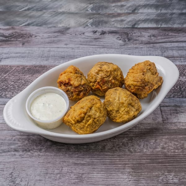 Five golden-brown fried appetizers with a side of ranch dipping sauce in a white dish on wood.
